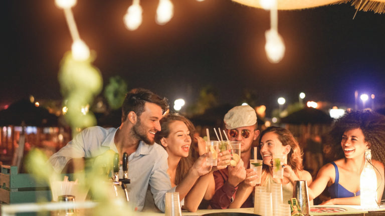 Happy friends cheering and drinking cocktails at beach party outdoor