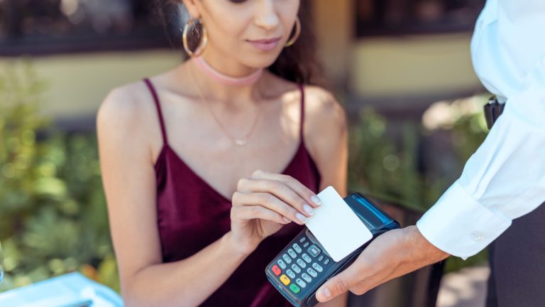 Close-up view woman using contactless credit card on pos terminal